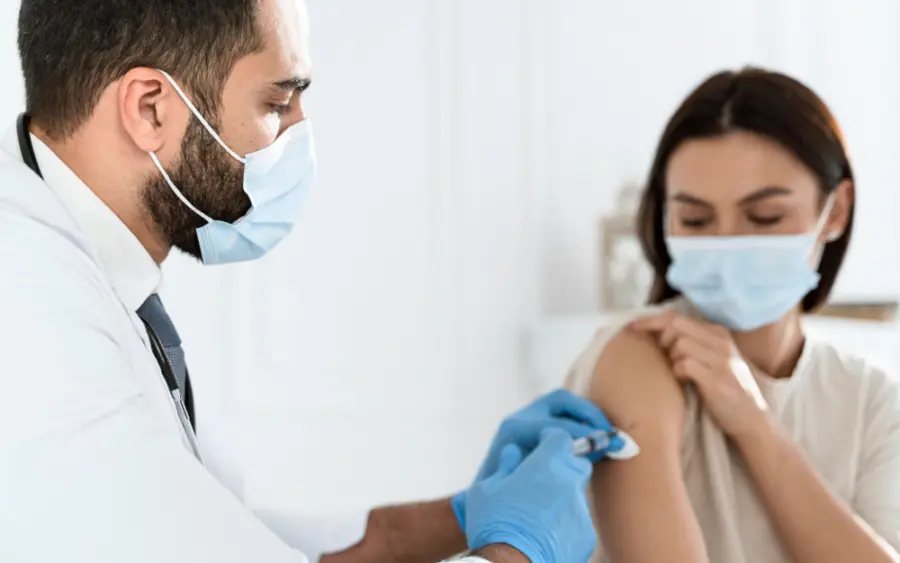 Pharmacist in a face mask and gloves preparing to vaccinate a woman's upper arm