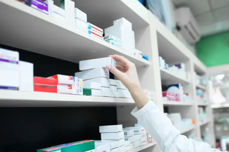 Pharmacist's hand taking a medicine box from a pharmacy shelf