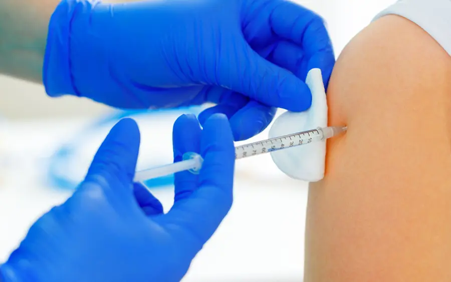 Gloved hands giving an injection in a person's upper arm